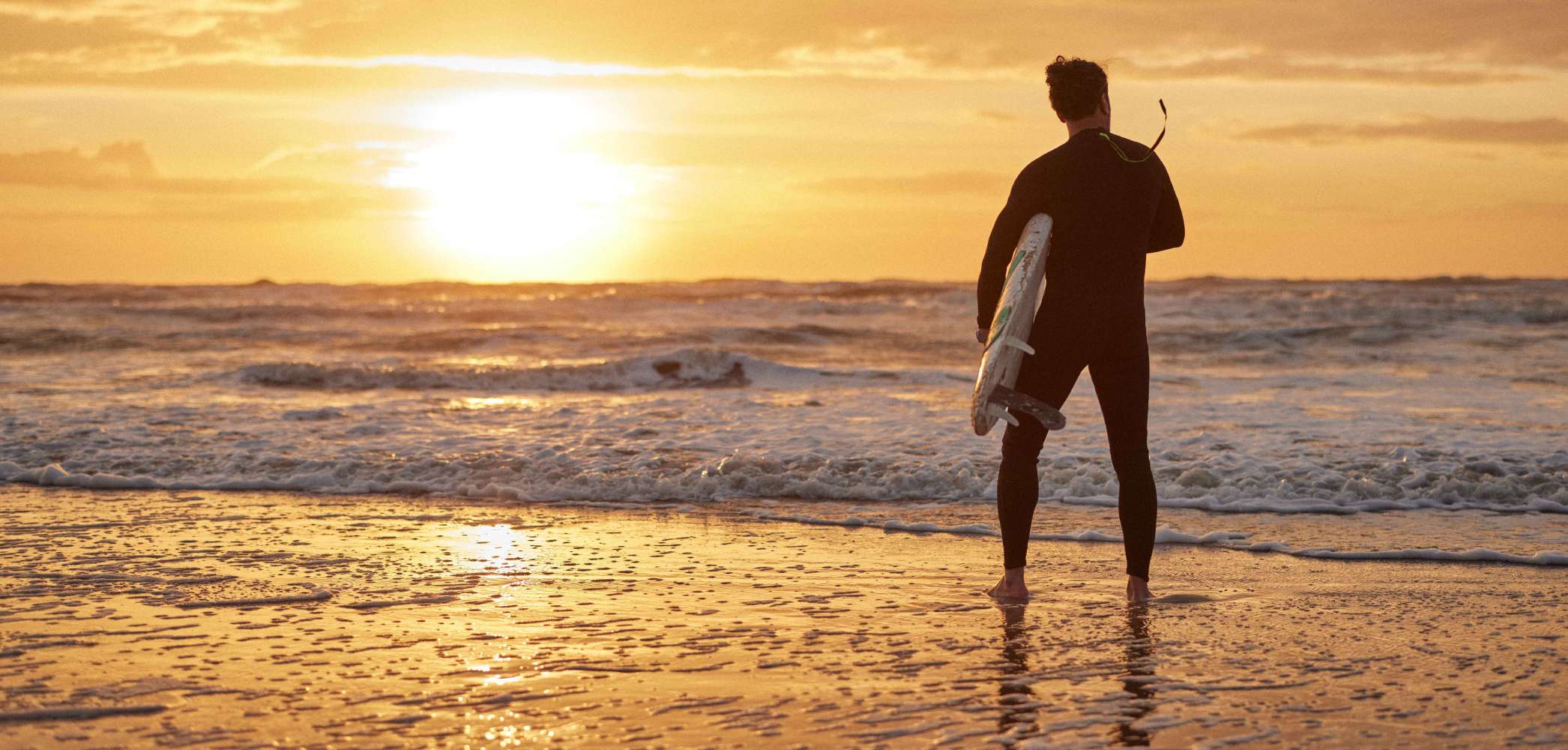 A surfer in his wetsuit analyzing the waves as the sun rises